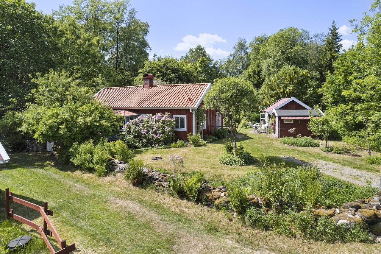 En gärdesgård och planteringar inramar boningshuset och dess små uthus.