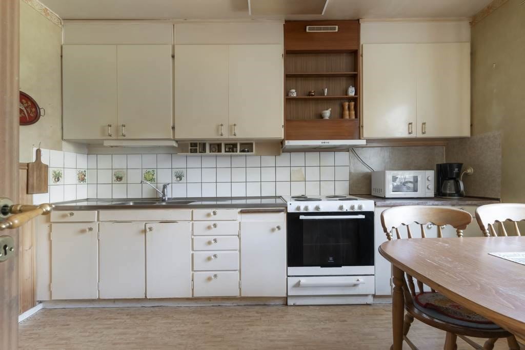 Ljust kök med vita köksluckor och kakel över diskbänk