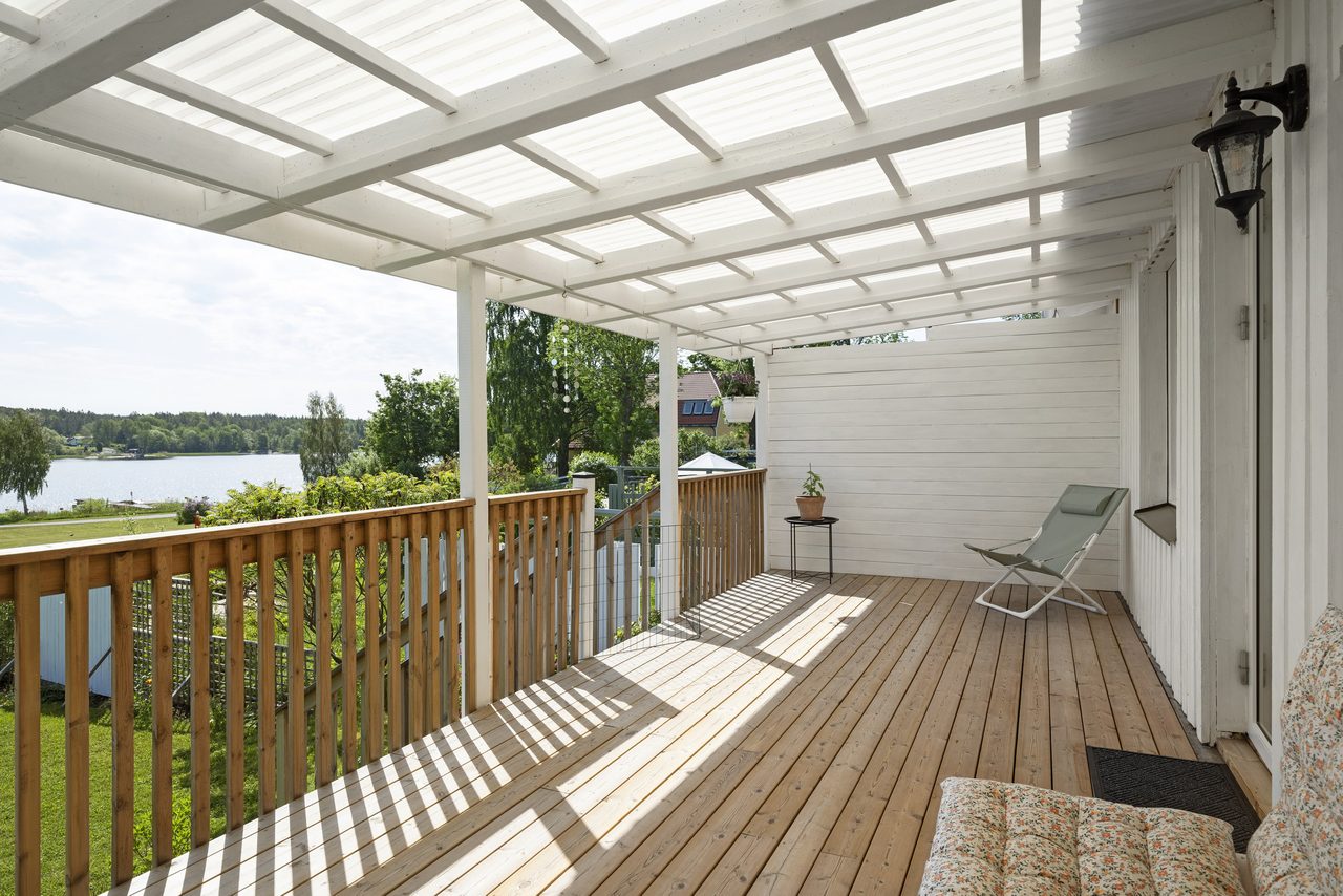 Altan under tak med trapp ned till trädgård.